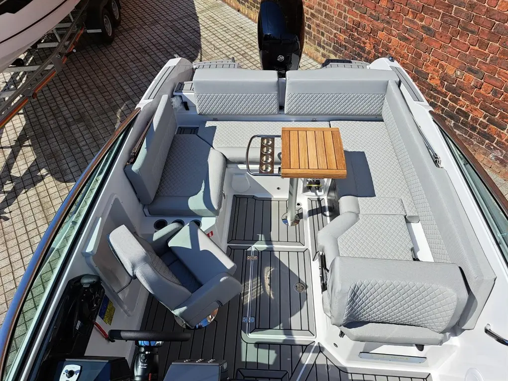 Aerial view of a modern boat interior featuring gray cushioned seating, a wooden table, and a steering console.